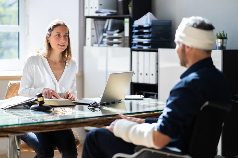 person with head and arm injuries meeting with an attorney at a desk