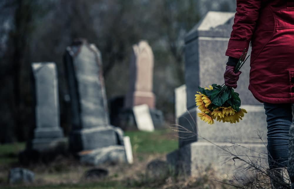 person carrying flowers while visiting a grave in a cemetery