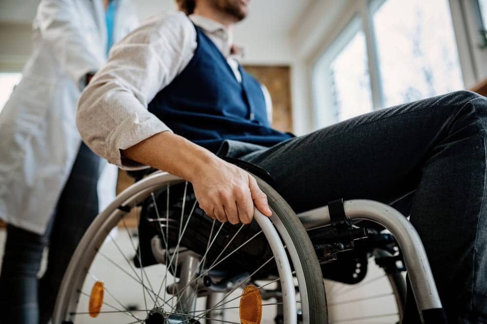 patient using a wheelchair while being assisted by a healthcare provider
