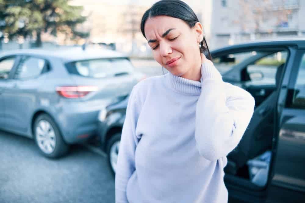 Woman holding her neck in pain while standing beside vehicles after a car accident